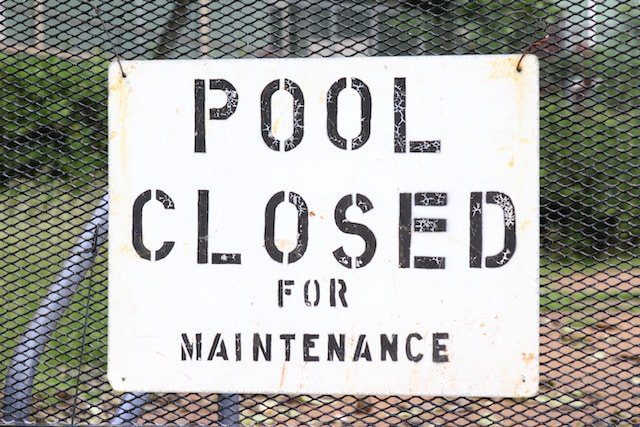 Sign reading “Pool Closed for Maintenance” on a metal fence.