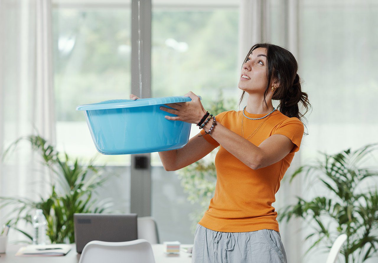 Woman catching water leak Woman catching ceiling leak water in a blue container.
