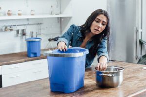 Woman catching water leak in kitchen using a bucket.