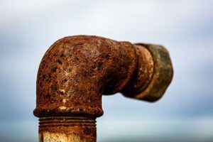 Close-up of a heavily rusted metal pipe elbow showing corrosion and surface damage.