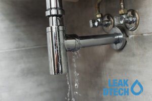 Chrome sink pipe visibly leaking water from a loose or damaged joint.