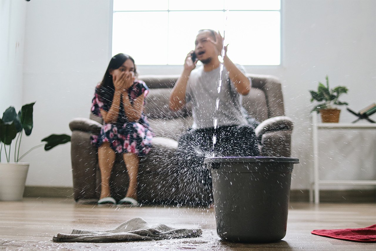 Family reacting to sudden indoor water leak spraying into a bucket