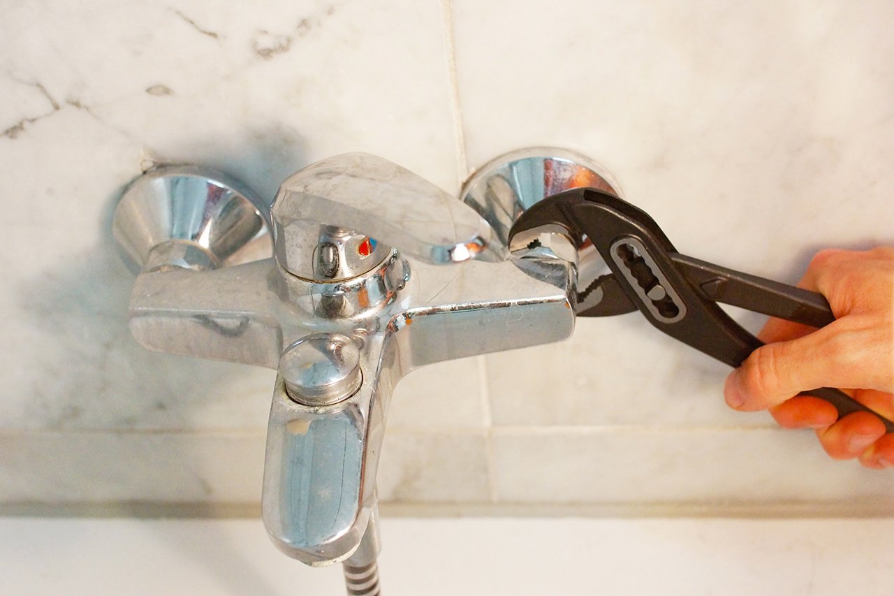 Technician tightening a leaking shower tap with a wrench