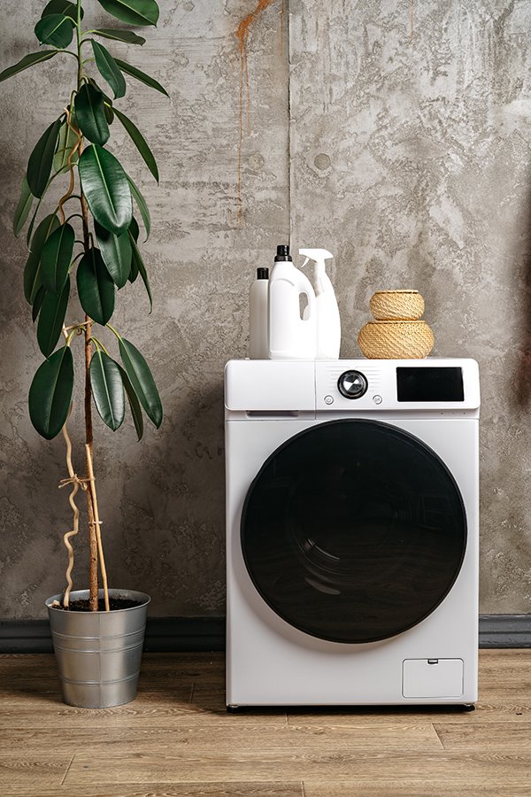 Front-load washing machine with detergent bottles in a laundry area.