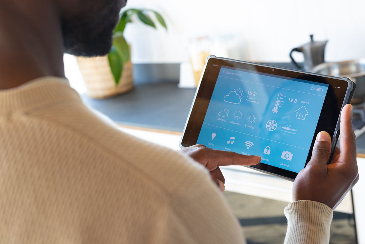 Person using a tablet displaying a smart home interface for temperature and device monitoring.