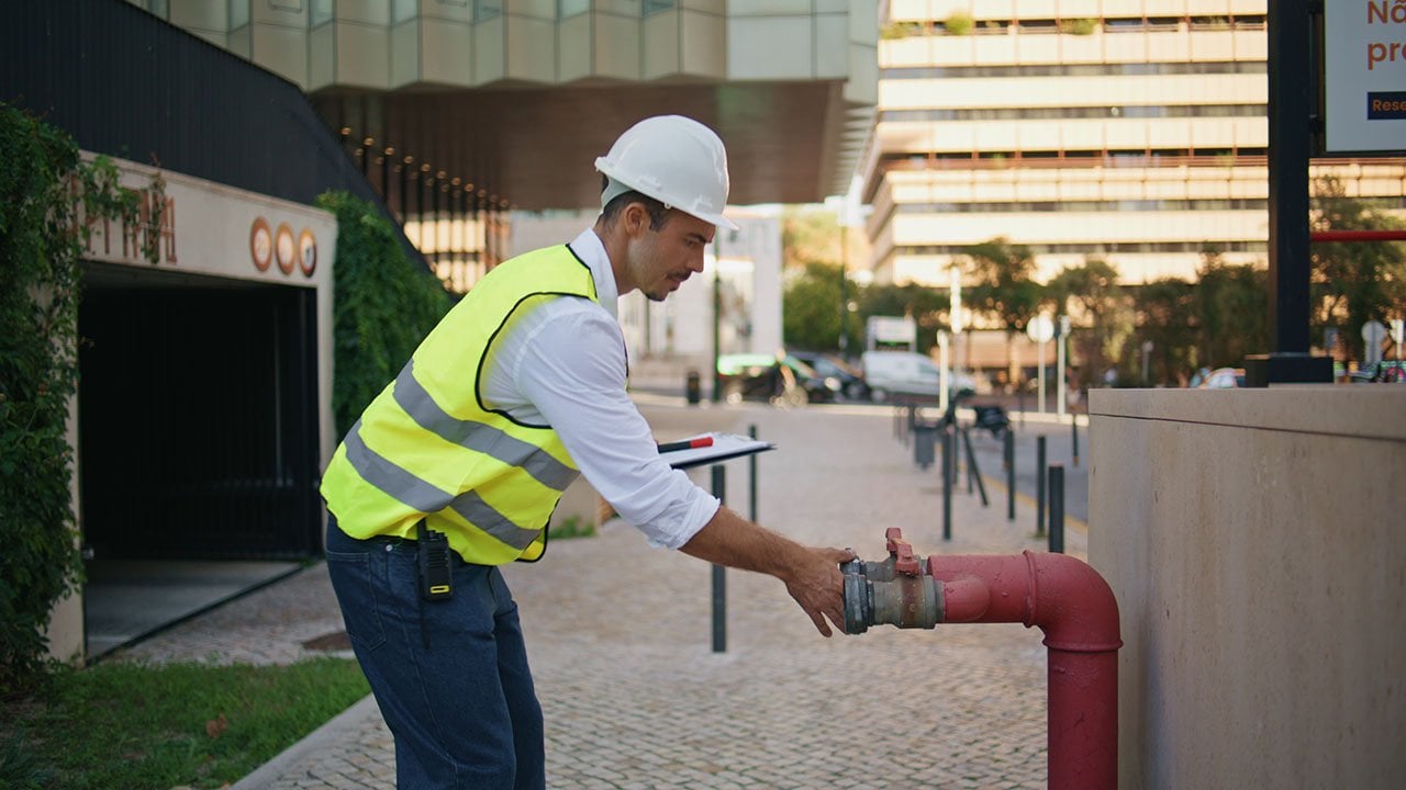 Engineer in high-visibility vest and hard hat inspecting an outdoor water valve or hydrant.