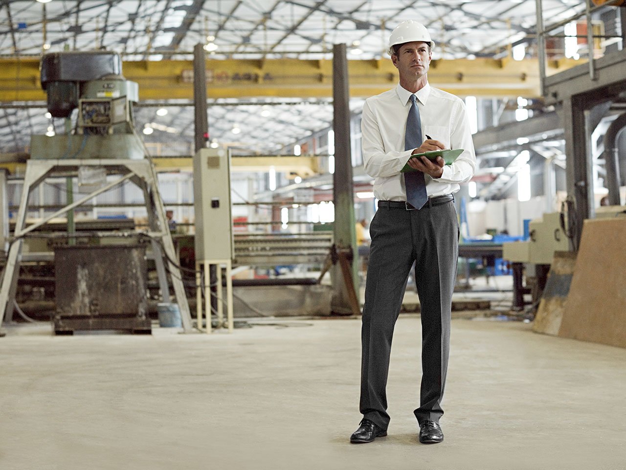 Engineer wearing a hard hat and holding a clipboard while inspecting an industrial facility.