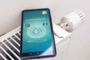 Smartphone displaying a water leak detection alert next to a household radiator.