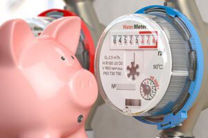 Close-up of a water meter beside a pink piggy bank representing high water bills from hidden leaks.