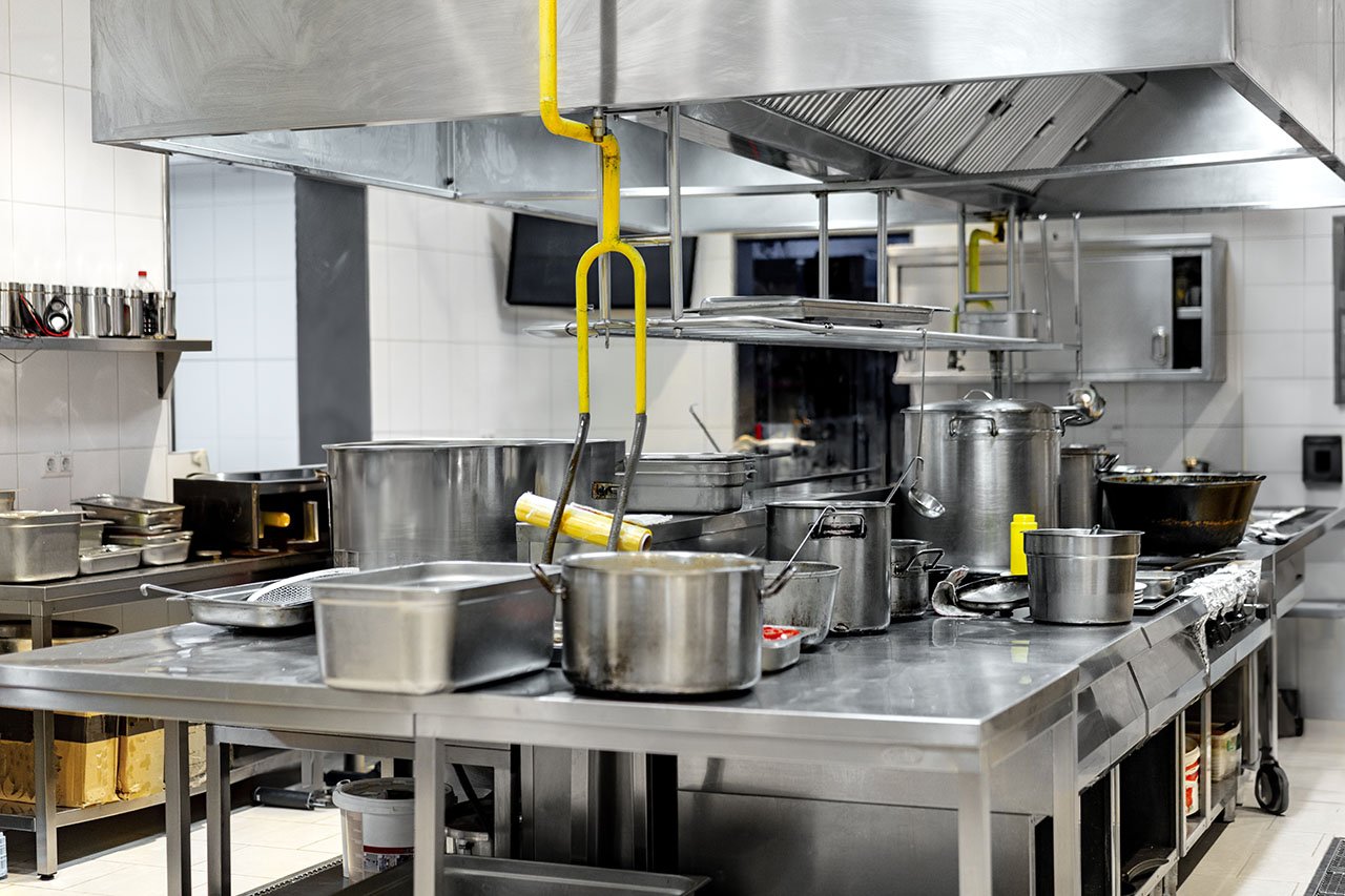 Busy commercial kitchen with stainless steel appliances showing potential leak-prone areas around sinks and cooking stations.