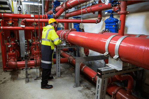 Worker inspecting red industrial pipelines in a petrochemical factory for leak detection