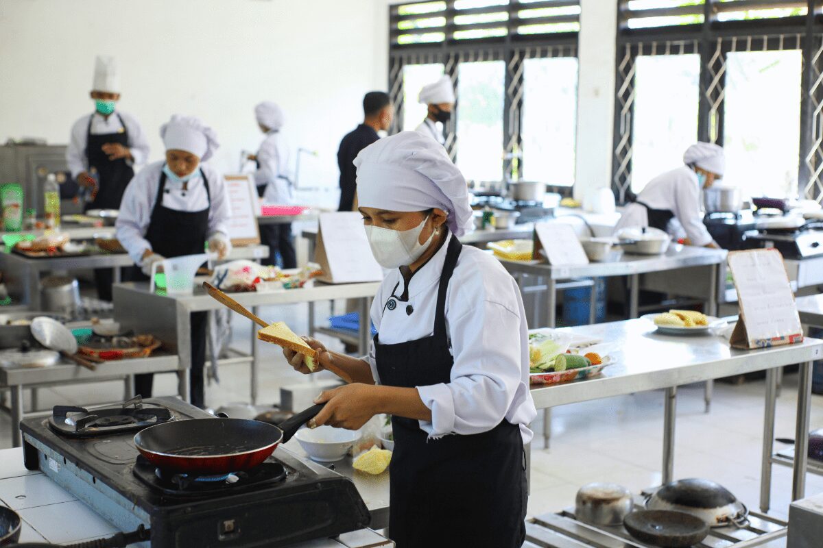 Chefs cooking in a commercial kitchen while wearing face masks