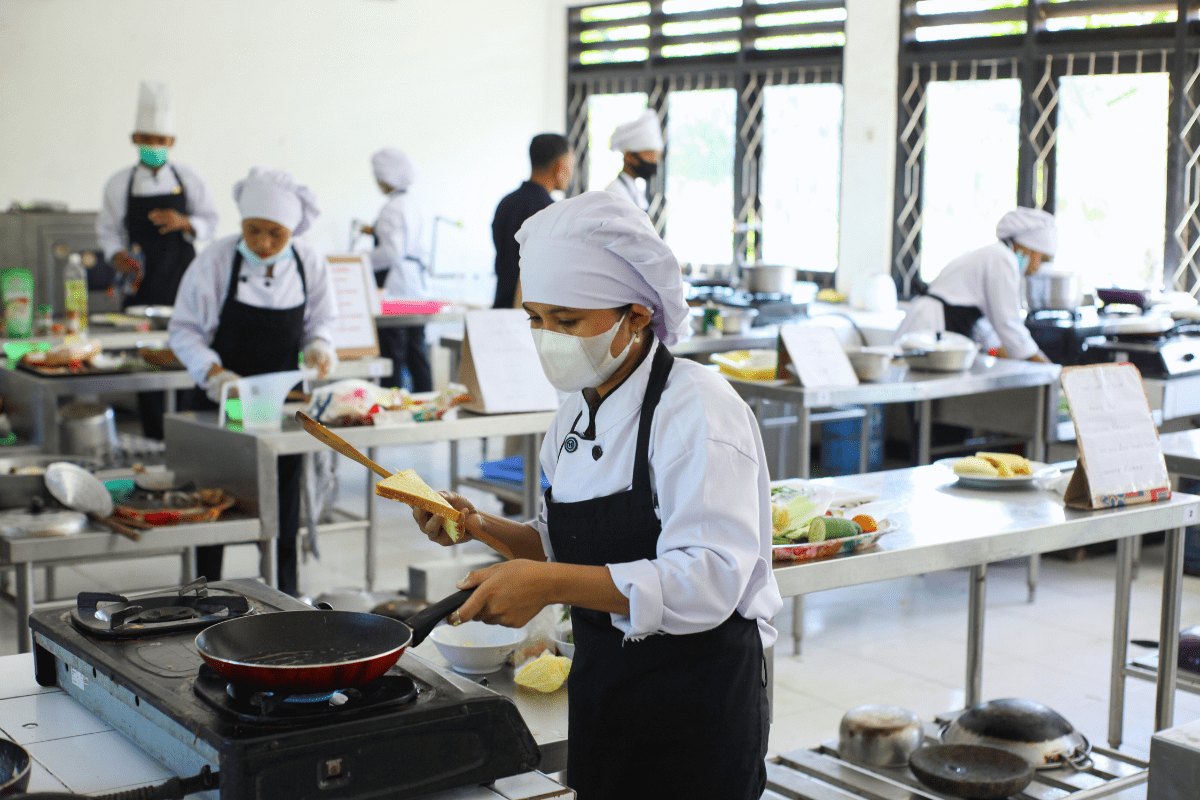 Chefs cooking in a commercial kitchen while wearing face masks