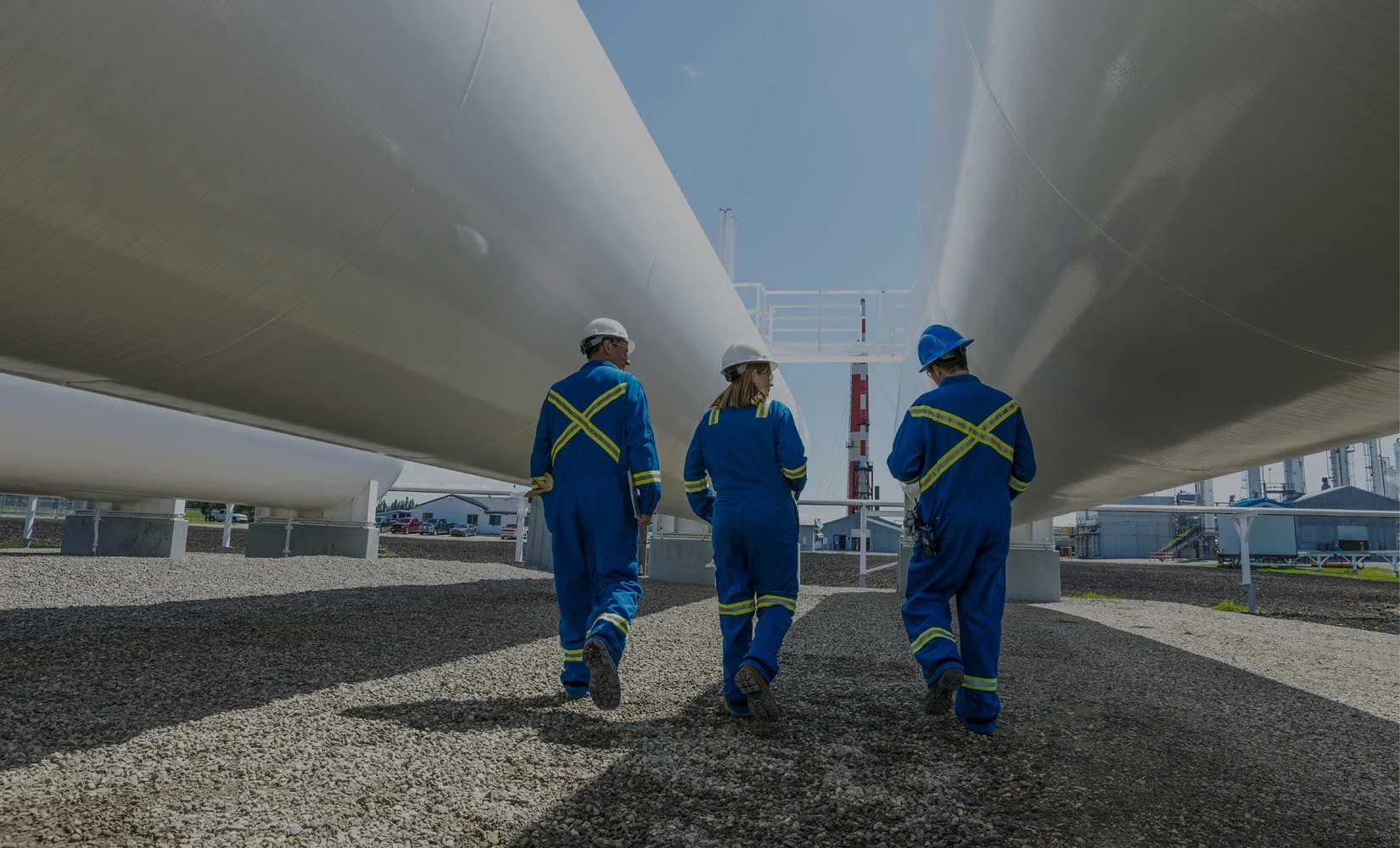 Industrial inspectors in safety gear examining large storage tanks and pipelines for leak detection in Dubai.